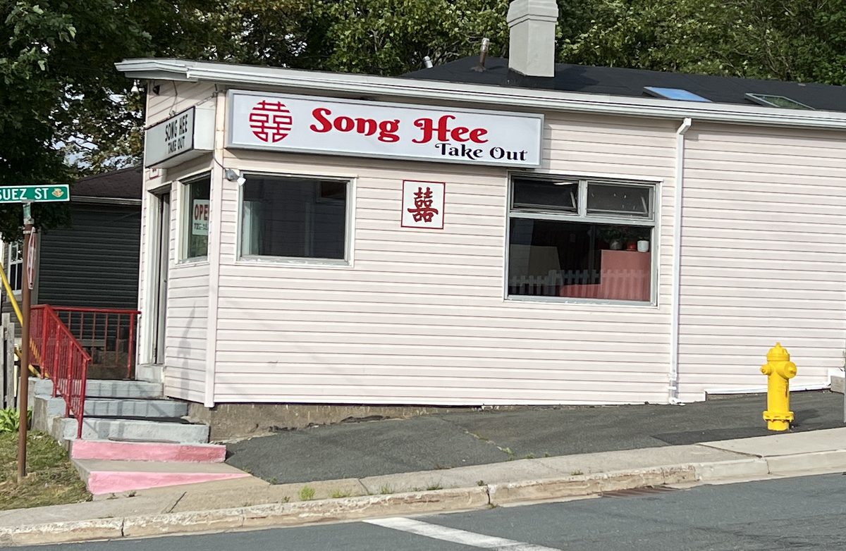 The Song Hee Take Out storefront: a small pink clapboard building with a red Song Hee sign at the corner of Empire Avenue and Suez Street